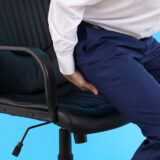 Man with bottom pain on blue background. Hemorrhoids concept