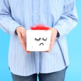 Woman holds toilet paper with feather on blue background. Hemorrhoids concept